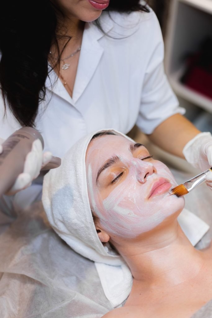 esteticista con un pincel aplica una mascarilla hidratante blanca la cara de un cliente joven en un salon de belleza spa
