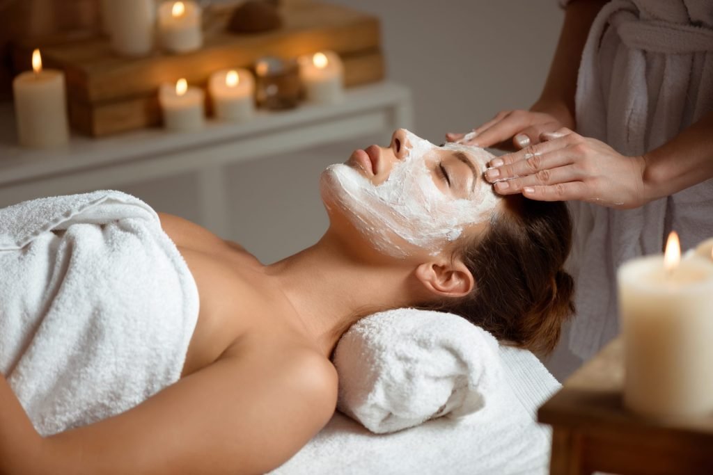 mujer joven en la mascara para la cara relajante en el salon de spa